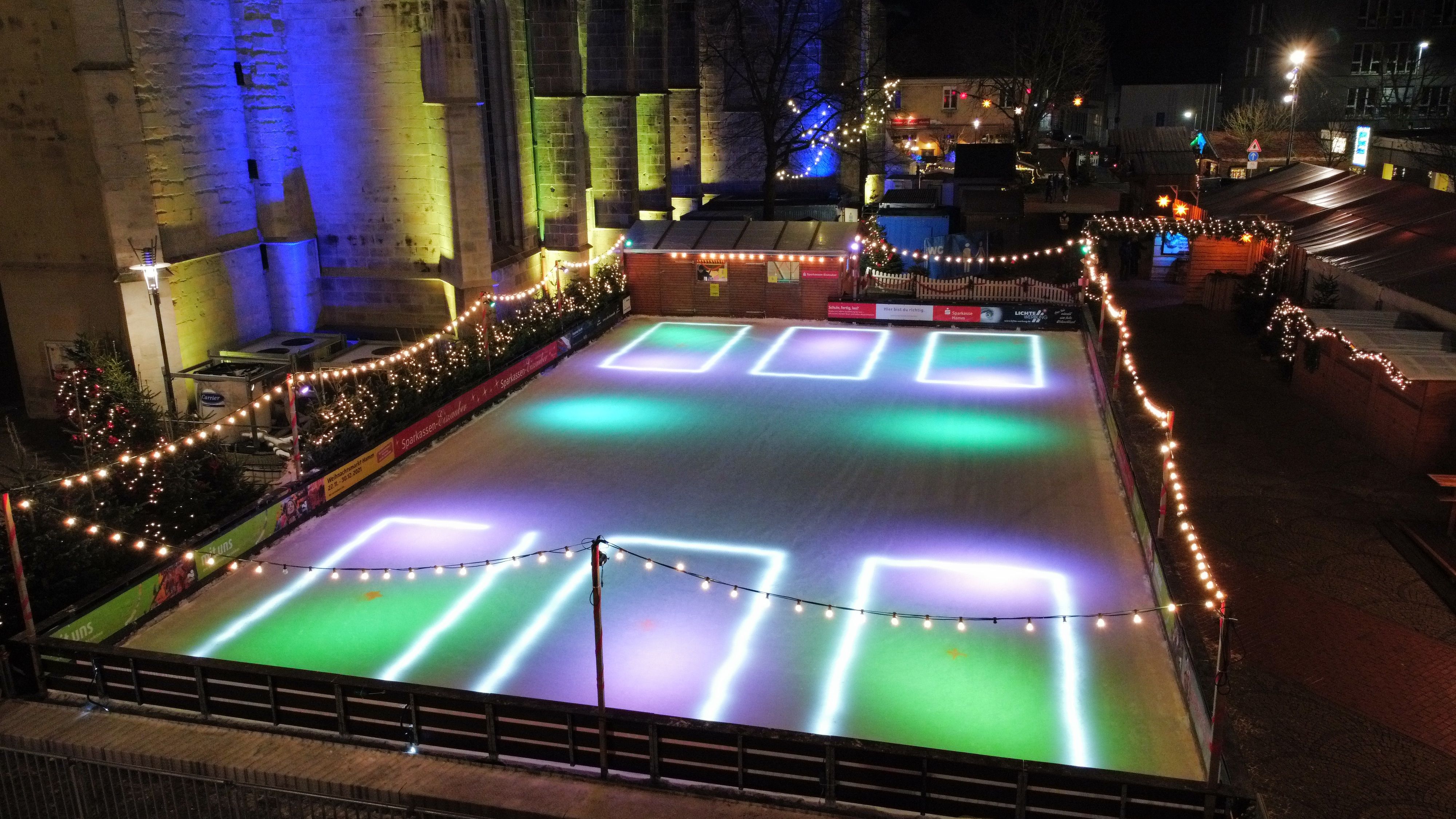 Een verlichte ijsbaan op de kerstmarkt in Hamm, omringd door feeërieke lichtjes en dennenbomen.