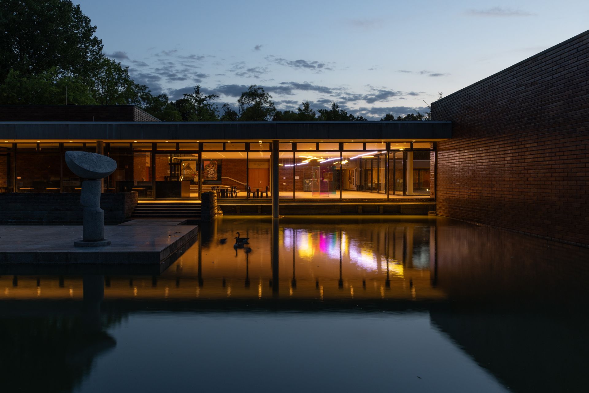 Het gedimde, warme licht in het interieur van het Museum voor Oost-Aziatische Kunst straalt de rustige esthetiek naar buiten uit. Grote glazen gevels bieden uitzicht op de Aachener Weiher