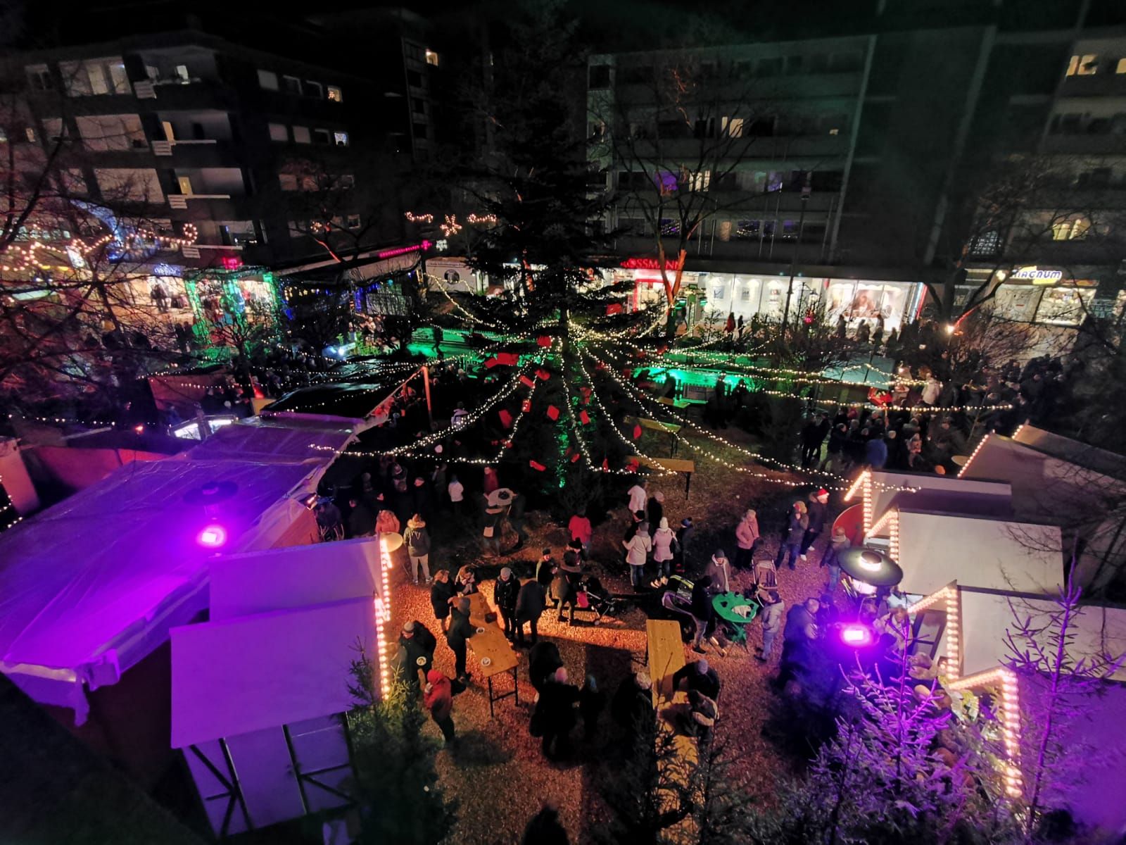 Luchtfoto van de kerstmarkt in Gronau bij nacht. Mensen wandelen tussen feestelijk verlichte kraampjes en een grote kerstboom.