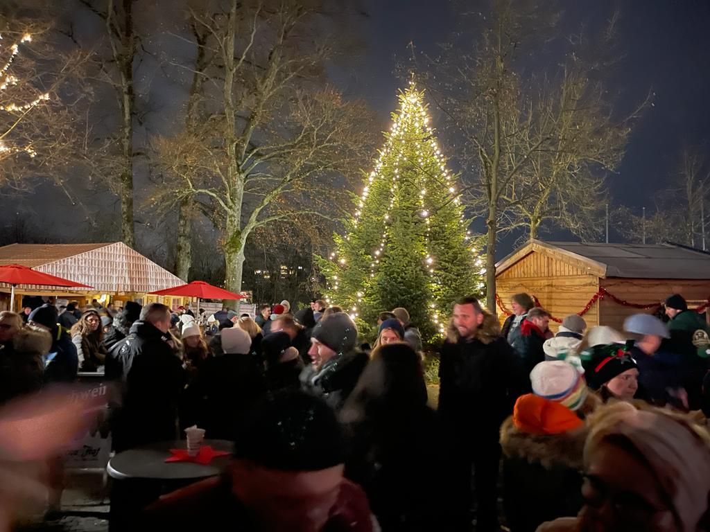 Drukte bij de Hückeswagen Hüttenzauber met verlichte kerstboom en houten hutjes op de achtergrond.