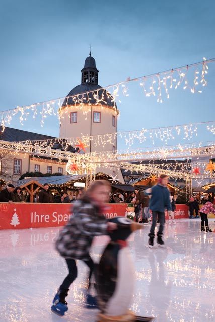 Schaatsers op de kerstmarkt van Siegen voor het Nederkasteel, omringd door feestelijke feeërieke lichtjes en kraampjes.