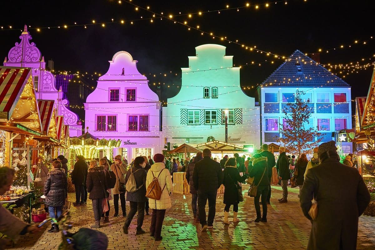 Feestelijk verlichte Sinterklaasmarkt in Burgsteinfurt bij nacht. Mensen slenteren tussen de kraampjes, kleurrijke lichtjes verlichten de gebouwen en zorgen voor een feestelijke sfeer.