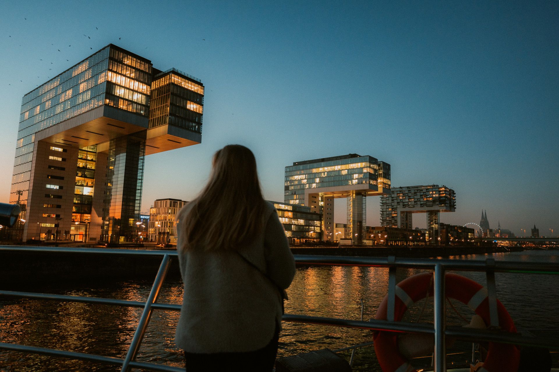 Frau schaut im Dunkeln von einem Schiff aus die beleuchteten Kranhäuser an