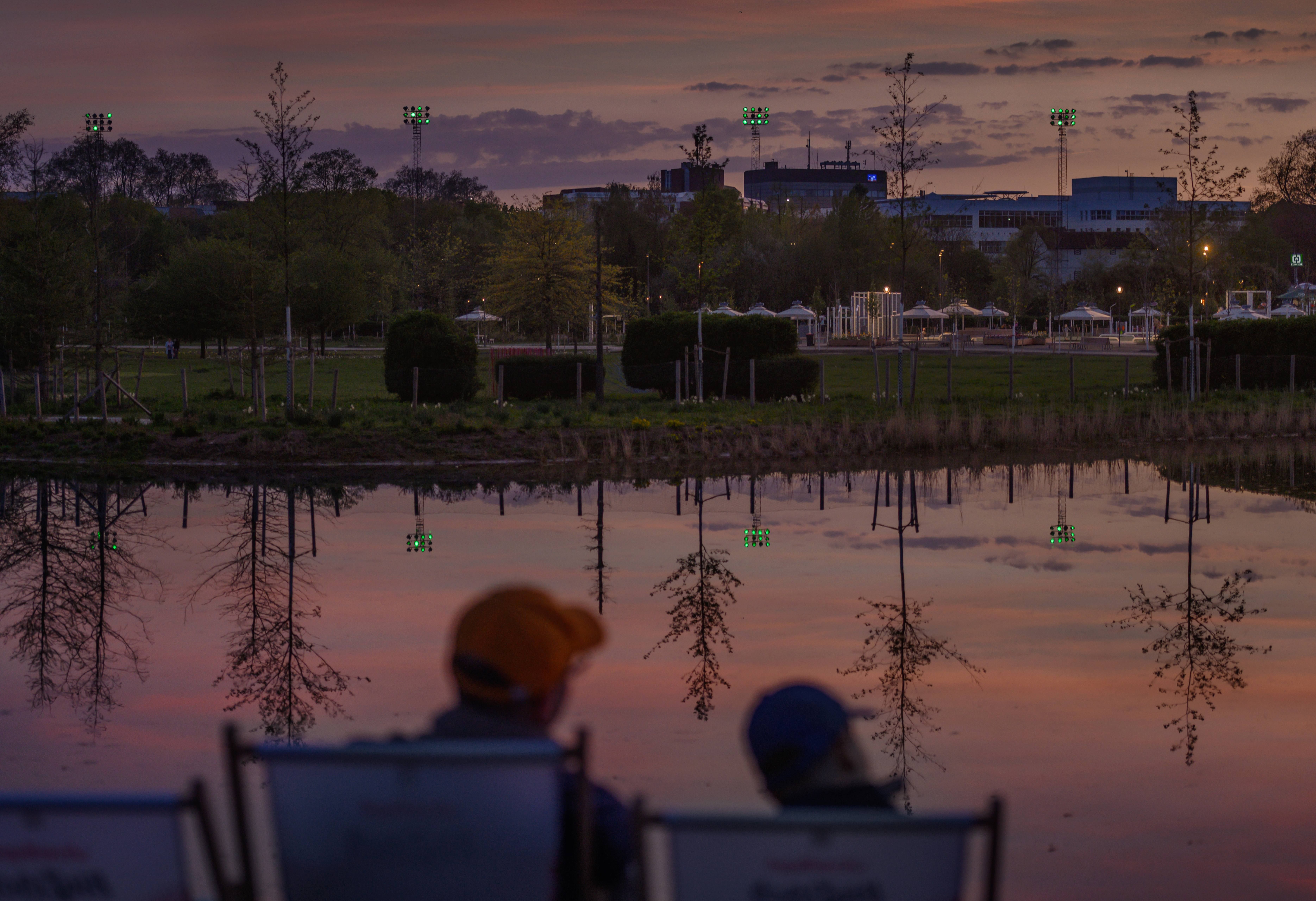 Twee mensen zitten in ligstoelen voor een meer bij zonsondergang op het terrein van de Neuss 2026 State Garden Show.