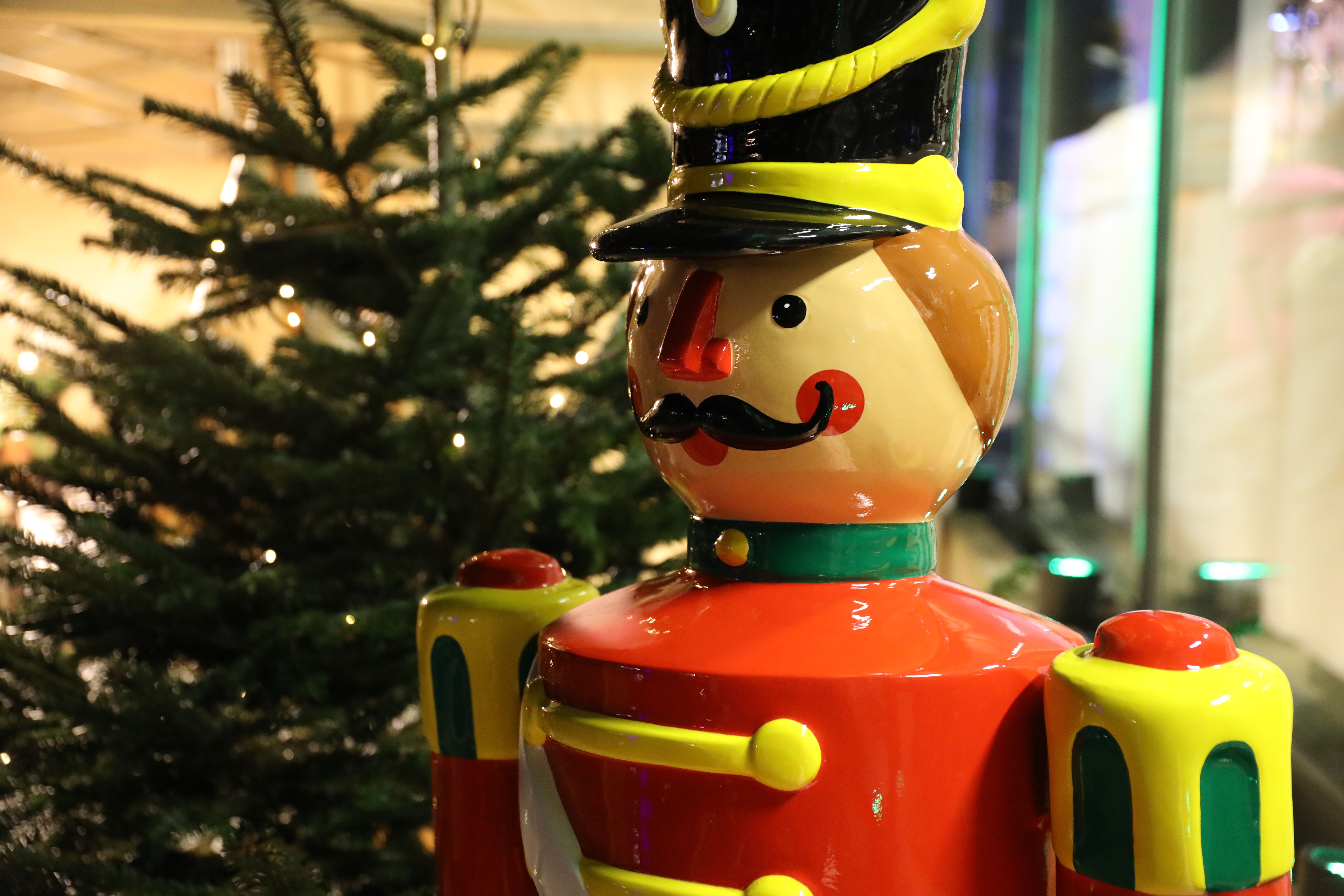 Een kleurrijke notenkraker staat voor een verlichte kerstboom.