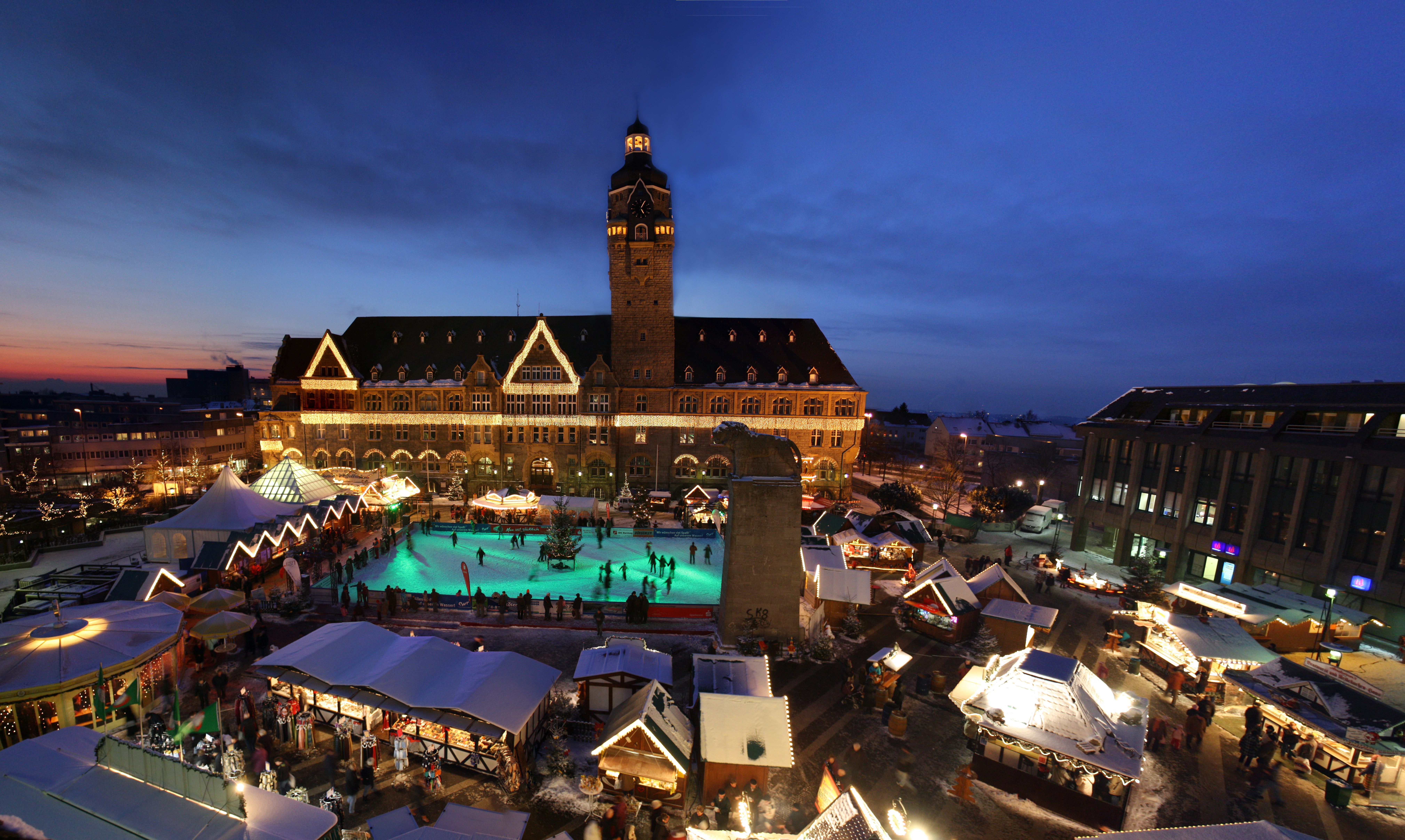 De kerstmarkt in Remscheid met verlichte kraampjes, een ijsbaan en het historische stadhuis in de schemering.