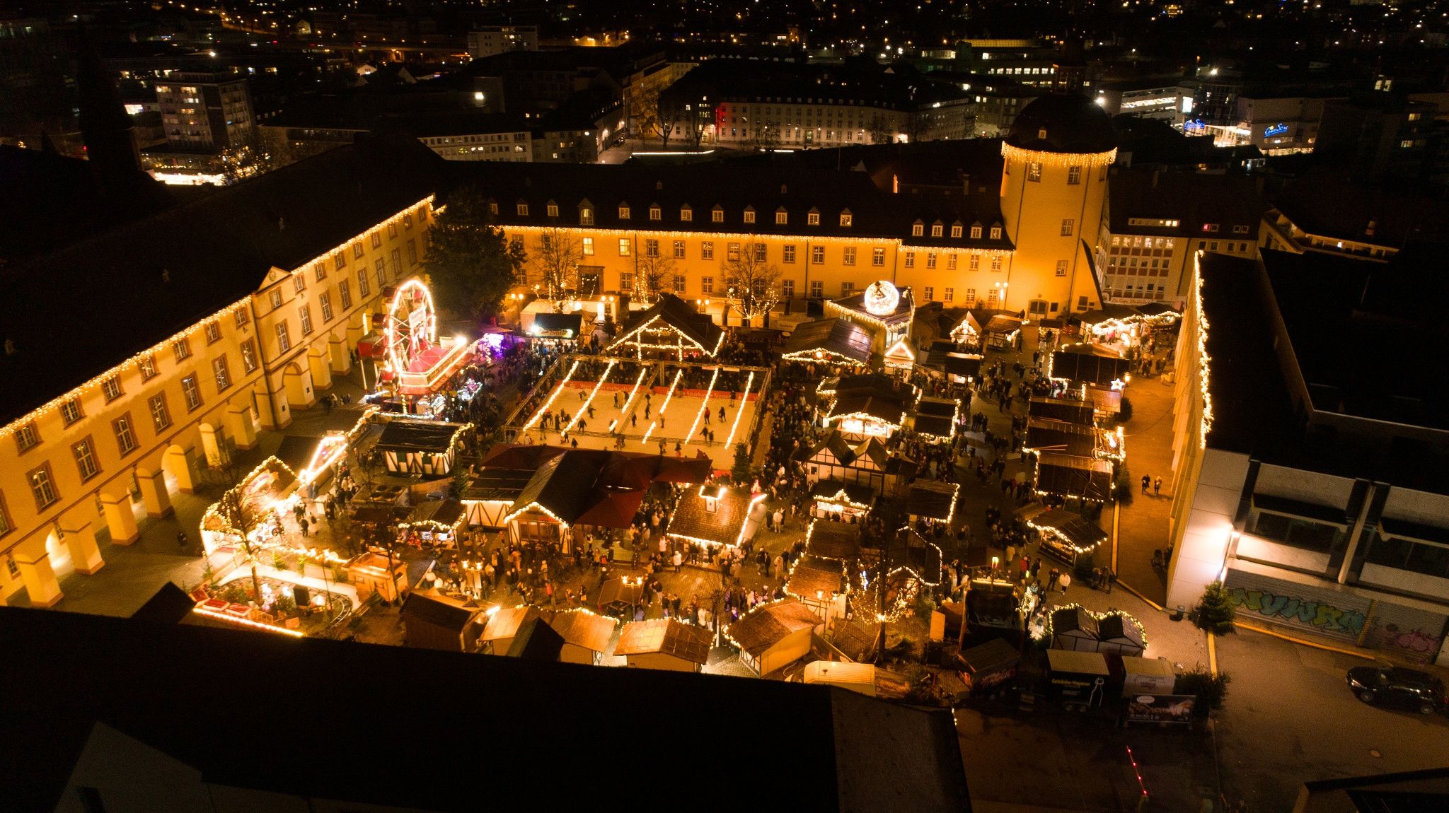 Luchtfoto van de kerstmarkt in Siegen bij het Lower Castle. De markt is feestelijk verlicht, met een ijsbaan en talloze kraampjes.