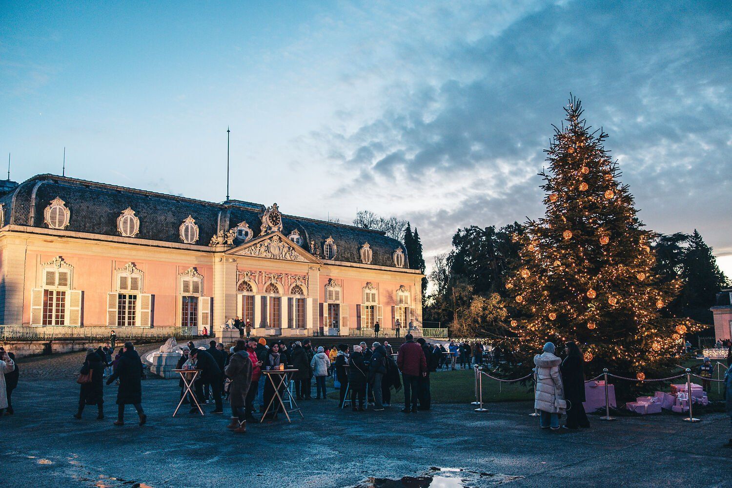 Kerstmarkt bij het kasteel van Benrath met een grote, verlichte kerstboom en bezoekers voor het barokke kasteel.