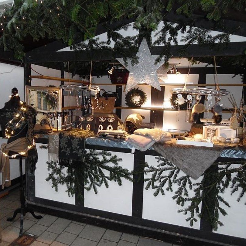 Een feestelijk versierde kerstmarktkraam met sieraden, sjaals en decoraties.