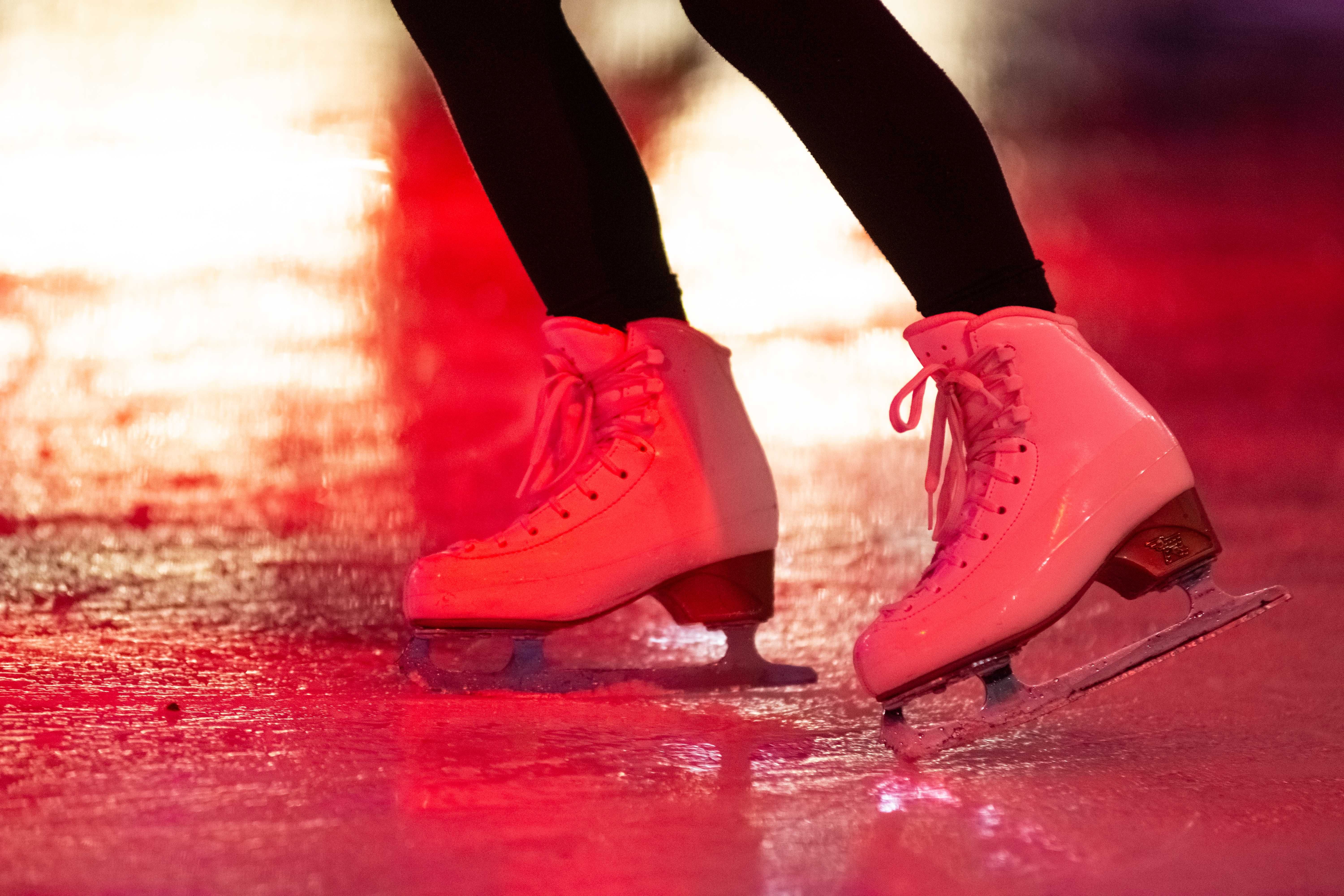 Witte schaatsen glijden over een rood verlicht ijsoppervlak.