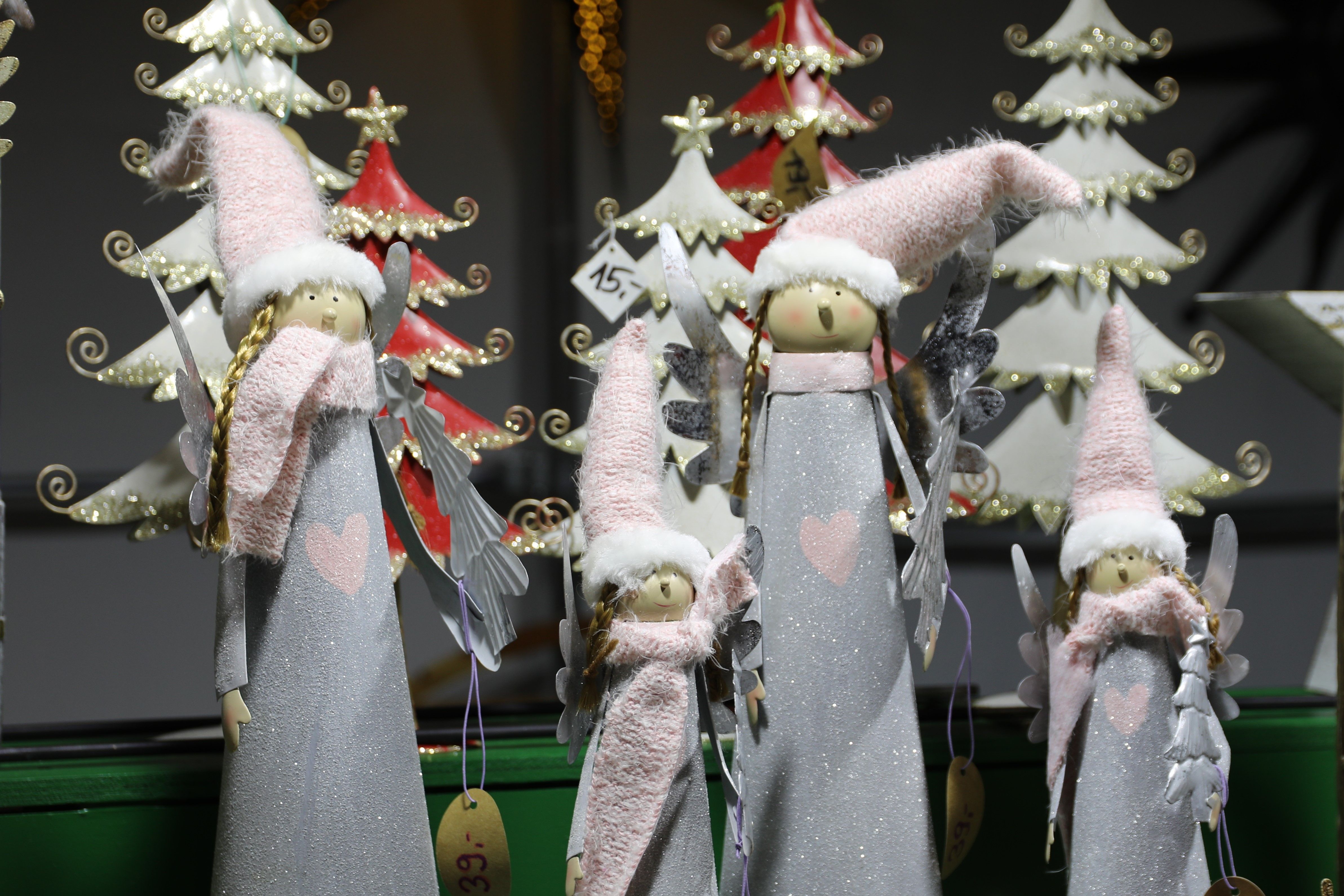 Kerstfiguren met roze hoeden en sjaals staan voor decoratieve kerstbomen.